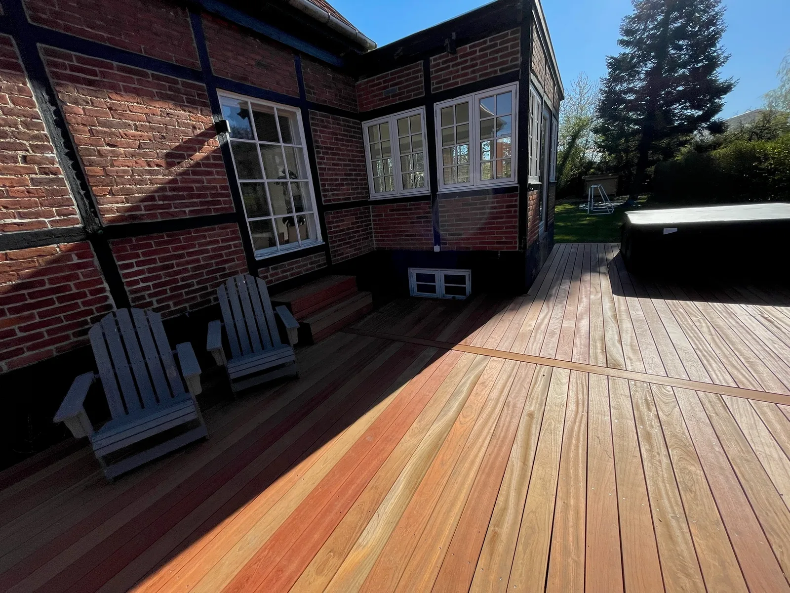 Terrasse i hårdttræ med loungestole ved et rødt bindingsværkshus