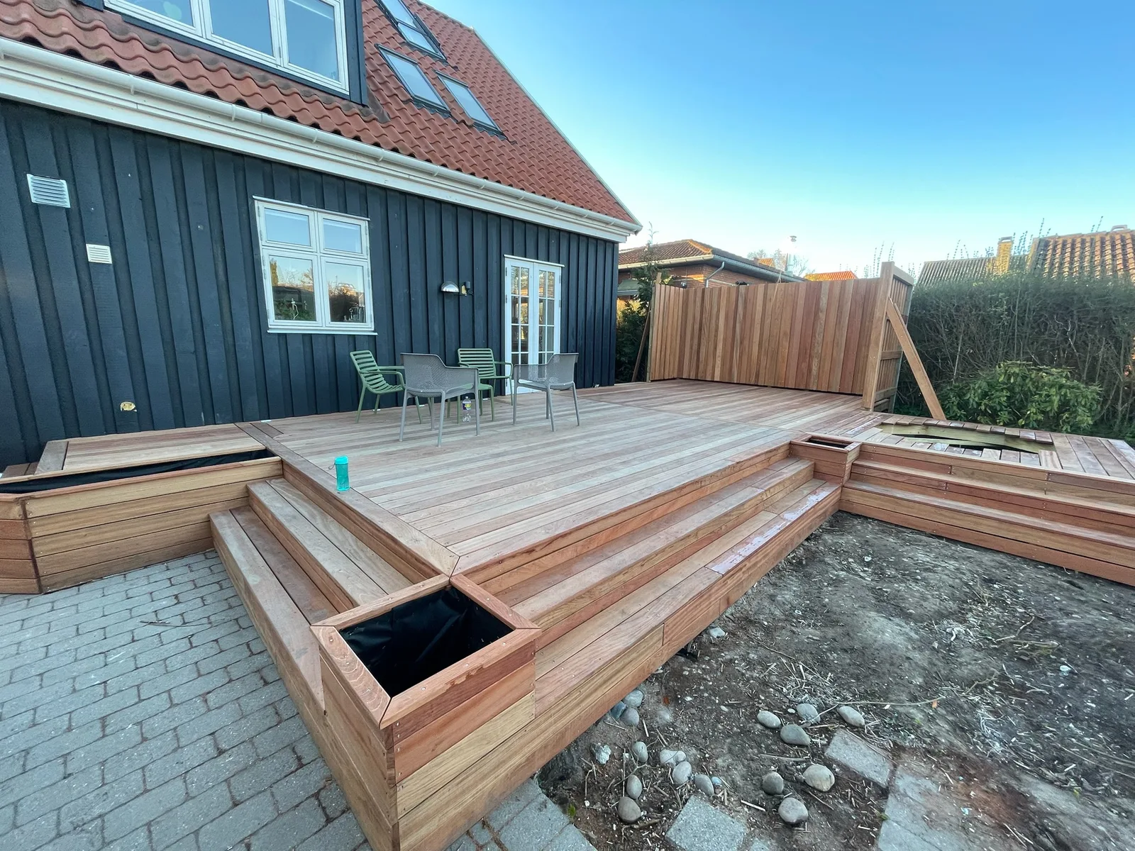 Terrasse i flere niveauer med brede trin og plantekasser ved et sort træhus